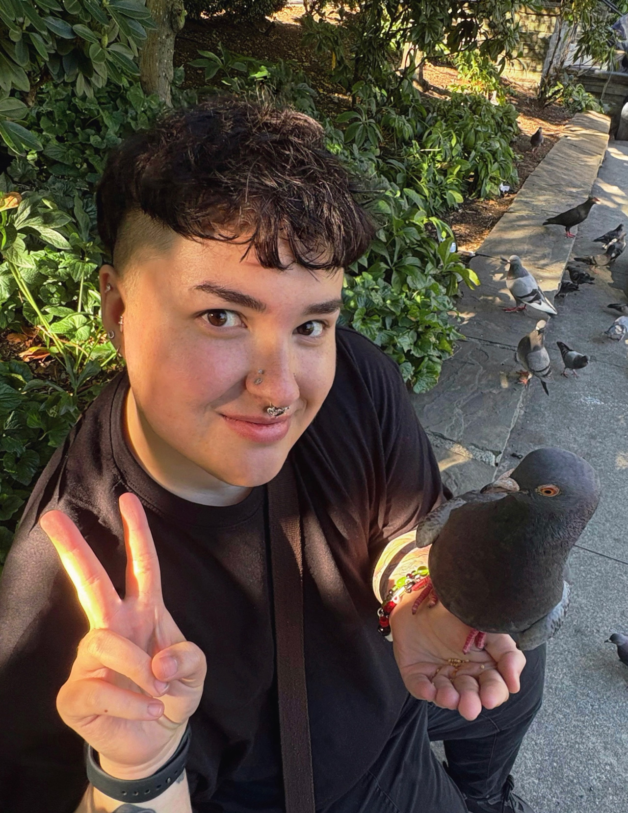 Self-portrait of Jordan Richert doing a peace sign with a pigeon in his other hand.